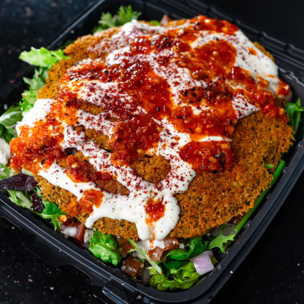 Mediterranean falafel dish topped with white sauce, red chili sauce, and spices, served over greens.