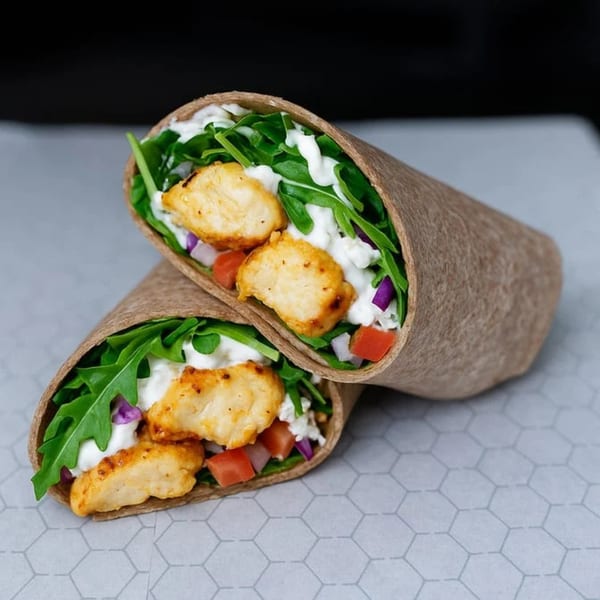 Two Kabsa Grill chicken wraps, filled with greens, tomatoes, red onions, and a creamy sauce.