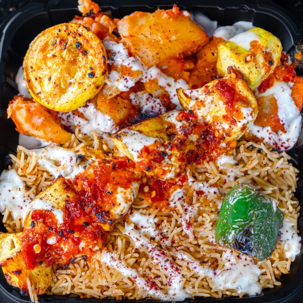 Kabsa Grill's Mediterranean dish with rice, chicken, roasted vegetables, and white sauce in a black container.