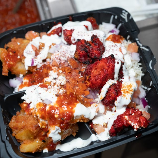 Kabsa Grill's Mediterranean dish with red chicken, white sauce, and rice in a black container.